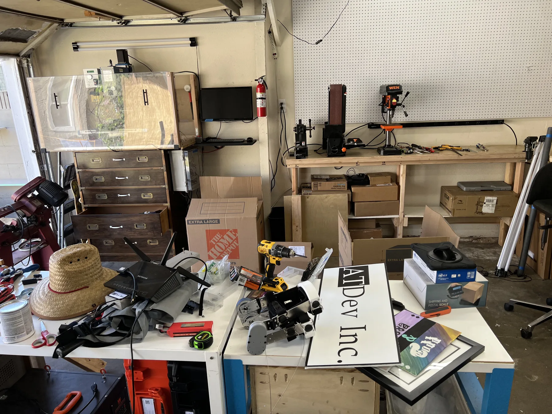 The AT Dev Inc garage workshop: workbenches with a drill press, belt sander and pegboard, a 3D printer enclosure, storage drawers and an AT Dev Inc sign