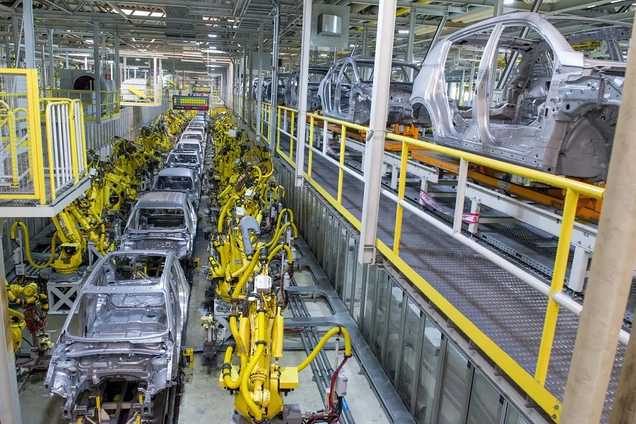 Yellow robots along the line, with car bodies on the overhead conveyor above