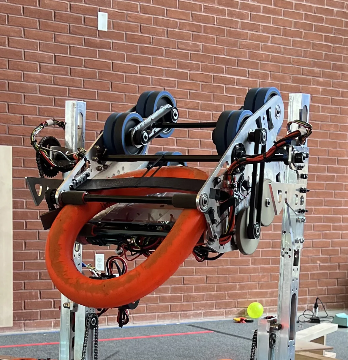 The 2024 shooter mechanism mounted on the robot, with blue flywheels and an orange note loaded, against a brick wall