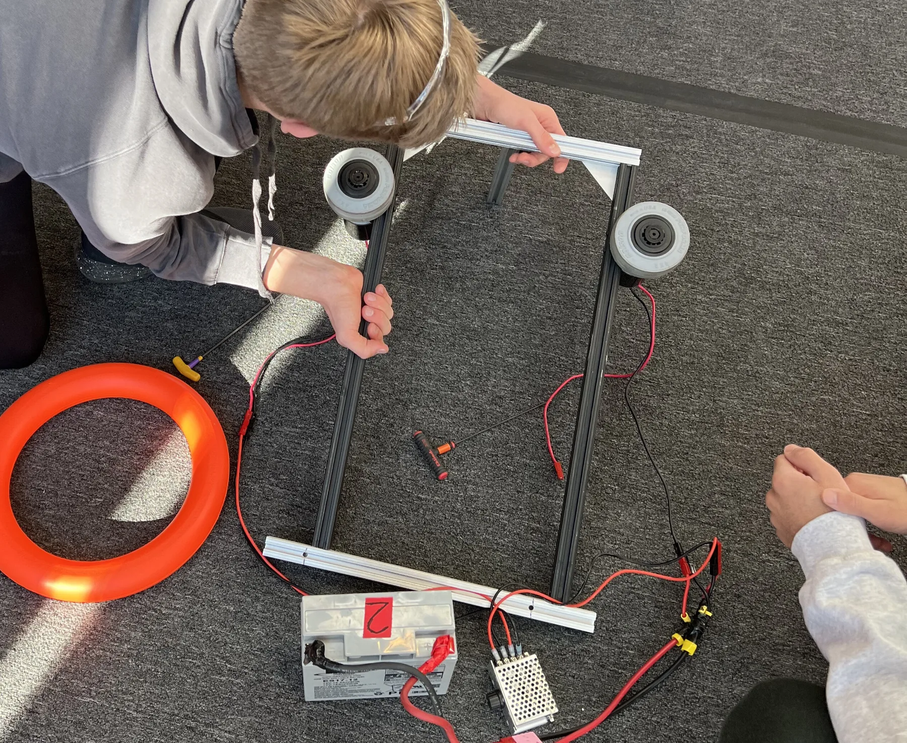 Shooter V1: a student assembling a bare flywheel test rig on the floor next to an orange note