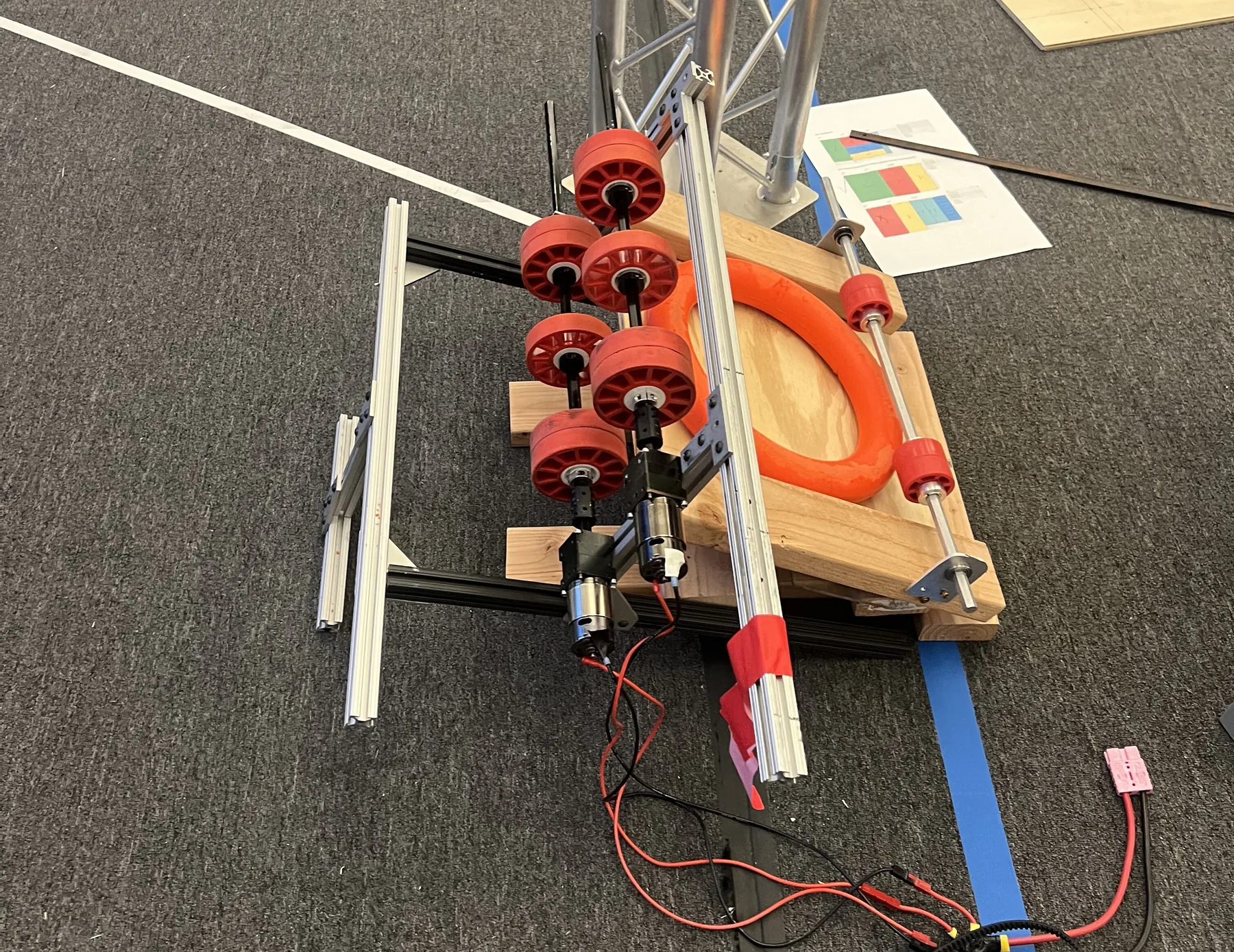 Shooter V2: wooden test rig with red wheels squeezing an orange note to measure compression