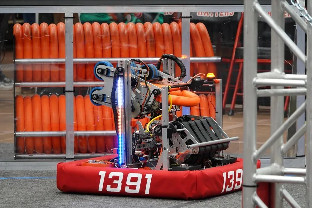 Team 1391's 2024 CRESCENDO robot with red bumpers numbered 1391, holding an orange note in its intake in front of an orange field structure