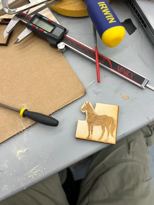 Digital caliper, screwdriver and an engraved horse silhouette panel on the workbench