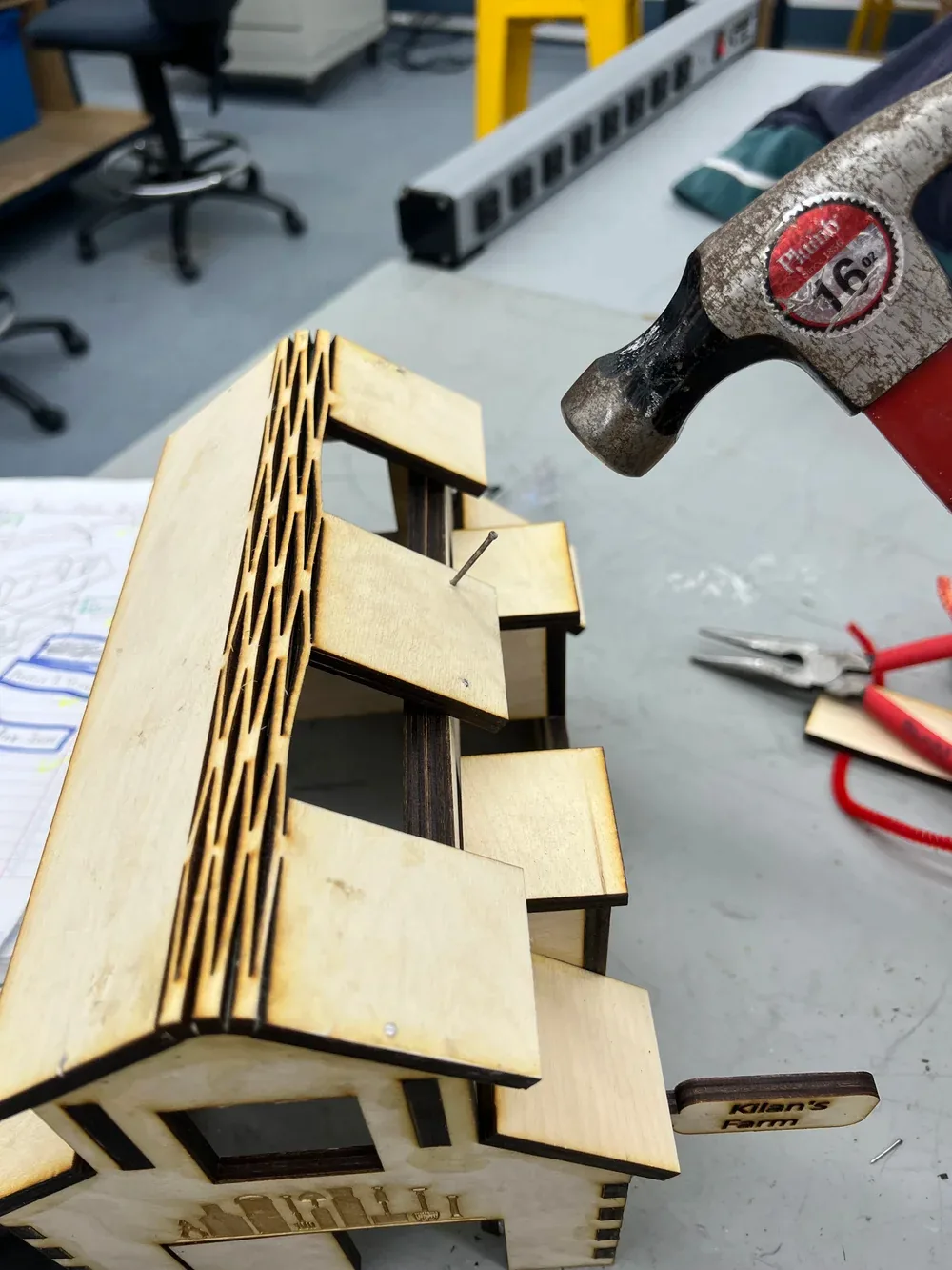 Hand holding the barn while a hammer drives small nails through the lattice roof into the body