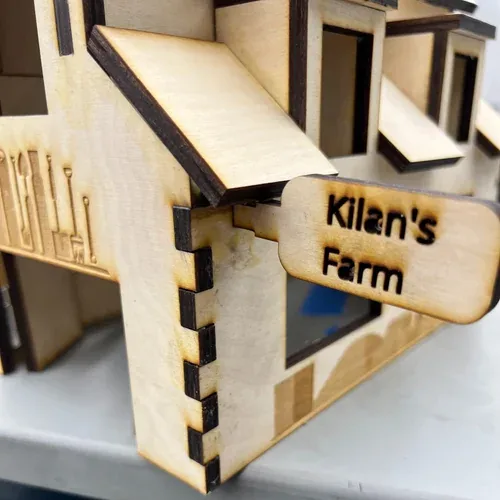 Close-up of the 'Kilan's Farm' sign fitted into the barn wall with a mortise-and-tenon joint next to a box-jointed corner
