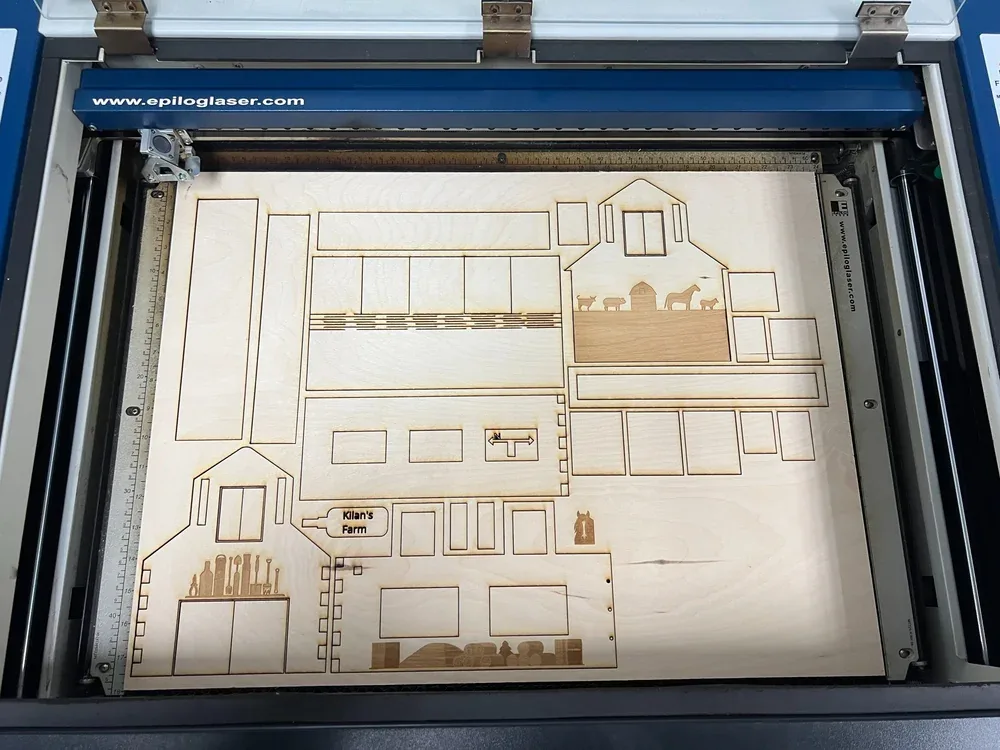 Epilog laser cutter bed with the nested barn parts cut and engraved into a plywood sheet
