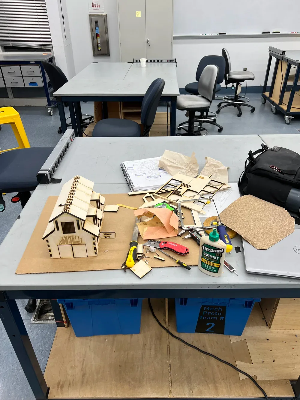 Workshop table covered with cut plywood parts, glue, pliers and the partly assembled barn