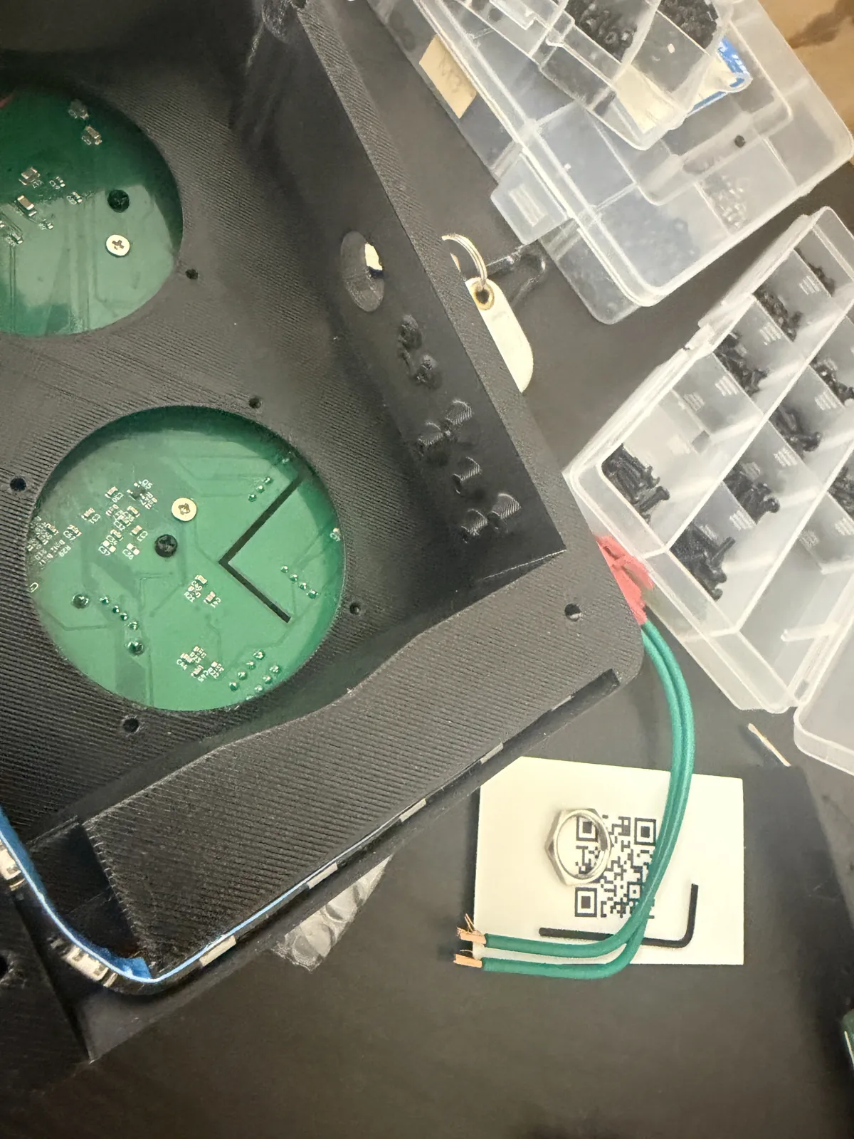 The bottom side of the board seen through the two round speaker openings in the back half of the printed enclosure, with the speaker leads and hardware boxes beside it