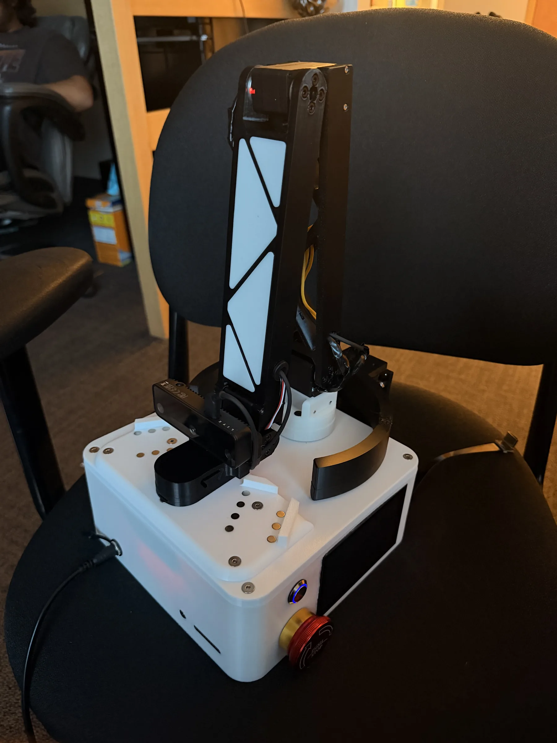V3 prototype clamped to a chair with the robotic arm folded down against the device body