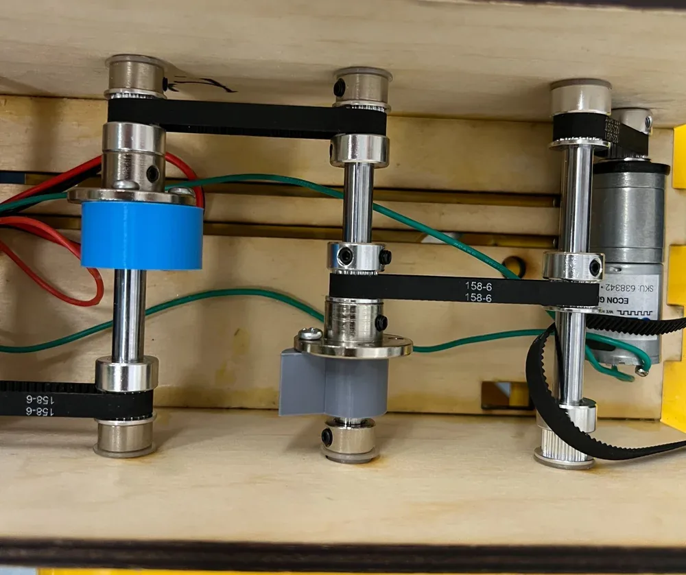 Inside the box: timing belts wrapped around metal pulleys on four vertical shafts, a blue 3D-printed pulley and the DC motor