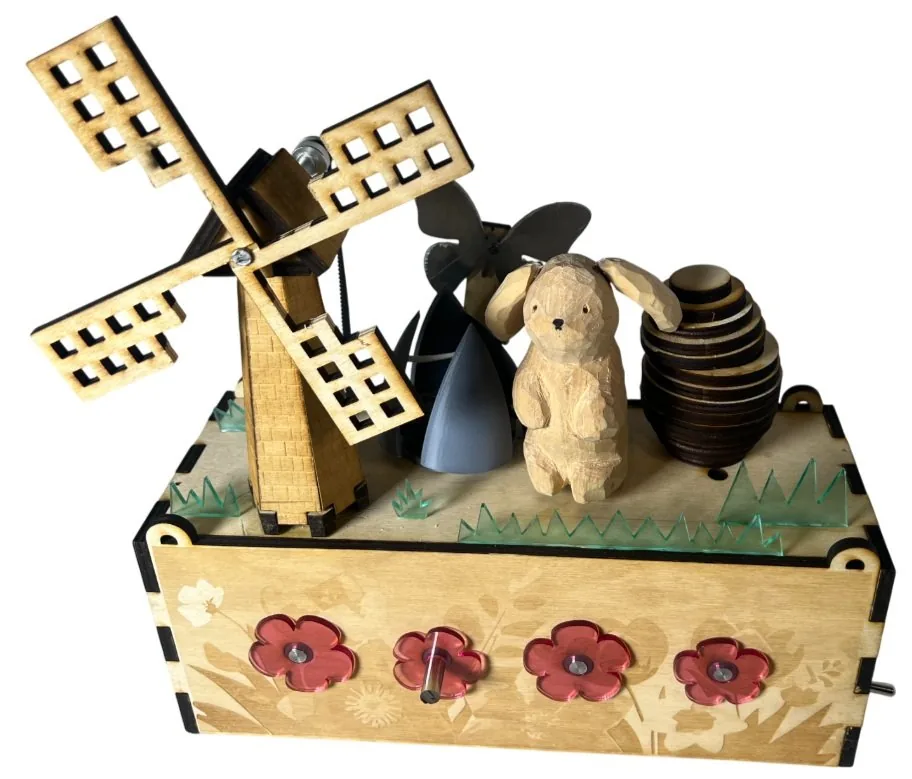 The finished Spring Cliches sculpture: a laser-cut wooden box with red flowers on the front, topped by a windmill, a butterfly, a carved bunny, a wooden egg and acrylic grass